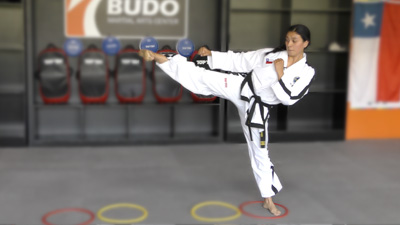 Advanced sparring drill showing Camila Urbina performing a side kick while training footwork and balance under the guidance of coach Ricardo Gonzalez