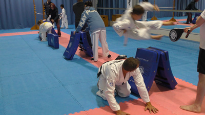 Kids practising Special Techniques in an ITF Taekwon-Do class, jumping over pads under the guidance of their instructor.